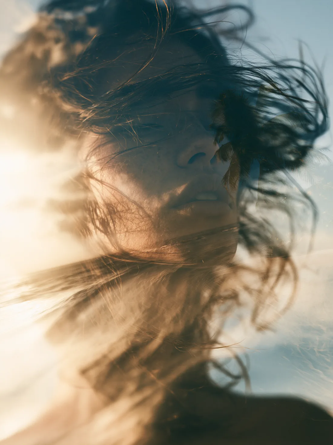 A resting face softly blended with palms, sunlight and clouds